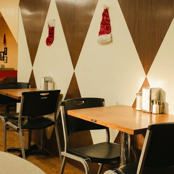 Restaurant interior with red and green booths, wooden tables, and Christmas decorations on patterned walls.