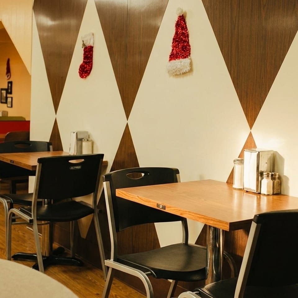 Restaurant interior with red and green booths, wooden tables, and Christmas decorations on patterned walls.